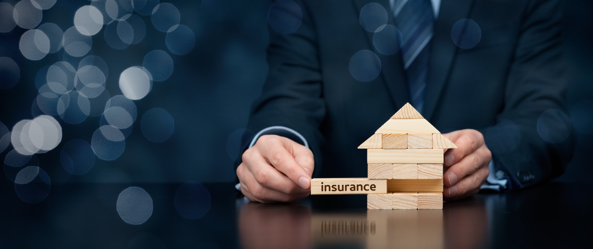 Property (family house) insurance protection concept. Insurance agent complete wooden model of the house with last piece with text insurance. Wide banner composition with bokeh background.